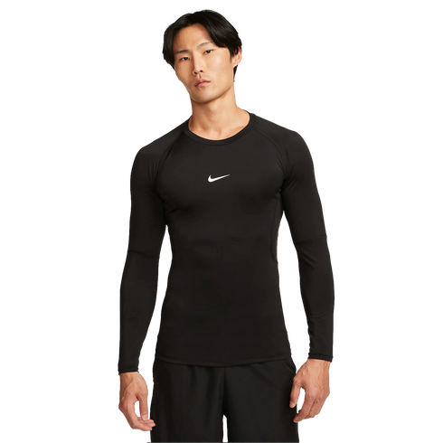A man wears a black long-sleeved Nike Pro compression top with a white swoosh logo and black shorts, standing against a plain white background.
