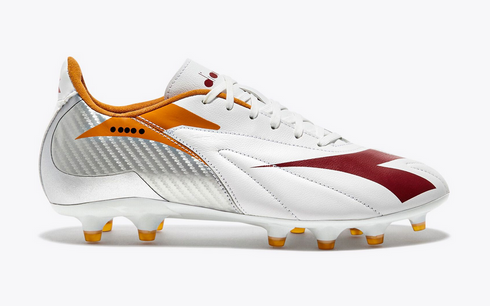 Side view of a white Diadora soccer cleat featuring maroon and orange accents, a silver textured heel, and a studded white sole.
