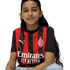 A smiling young girl with long dark hair sits against a white background wearing a red and black striped AC Milan soccer jersey.