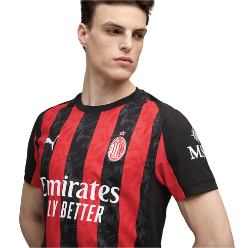 A young man models the red and black striped AC Milan home jersey, featuring the club crest and sponsor logos.