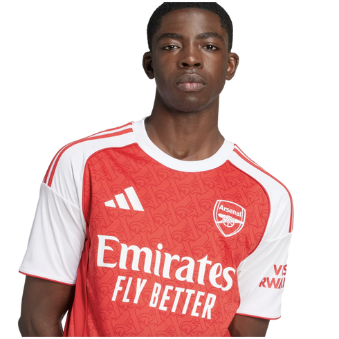 Portrait of a young Black man wearing an Arsenal FC home football shirt against a white background.