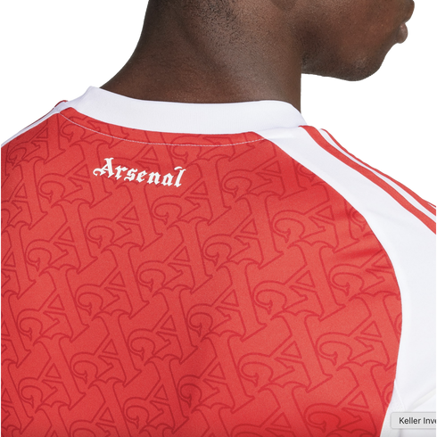 Close-up of the back of a red Arsenal jersey with white gothic-style text reading "Arsenal" and a repeating "A" monogram pattern across the fabric.