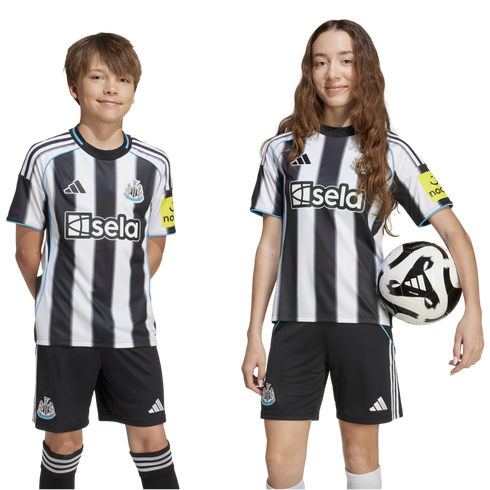 A boy and girl wearing black and white striped Newcastle United home kits smile against a white background. The girl holds a soccer ball. They look directly at the camera.