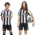 A boy and girl wearing black and white striped Newcastle United home kits smile against a white background. The girl holds a soccer ball. They look directly at the camera.