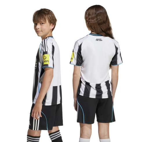 Two youth models wearing a black and white striped soccer kit. The girl displays the back with 'HOWAY THE LADS' text, and the boy faces sideways.