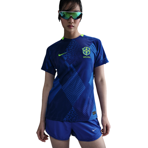A person wears a blue Nike Brazil national team soccer jersey with leopard print patterns, matching shorts, and iridescent sports sunglasses against a white background.