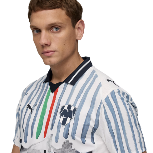 A man in a white Puma football jersey featuring light blue brushstroke stripes, a central green and red stripe, and the Monterrey club crest.