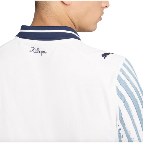 Close-up back view of a white Puma x KidSuper shirt with a navy striped collar, "KidSuper" script logo, and a Puma logo on the shoulder.