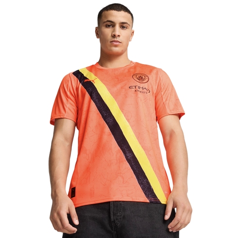 A young man wearing an orange Manchester City football jersey with a black and yellow diagonal sash.