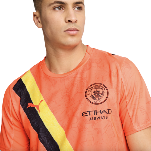 A man wearing an orange Manchester City soccer jersey featuring a diagonal black and yellow sash, the club crest, and the Etihad Airways sponsor logo.