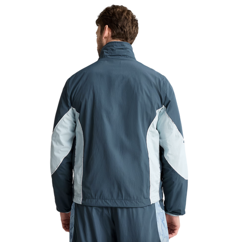 Back view of a man wearing a blue and light blue paneled athletic jacket and matching shorts.