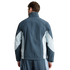 Back view of a man wearing a blue and light blue paneled athletic jacket and matching shorts.