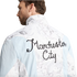 Rear view of a man in a light blue and white marbled jacket with "Manchester City" embroidered in black cursive script on the back.