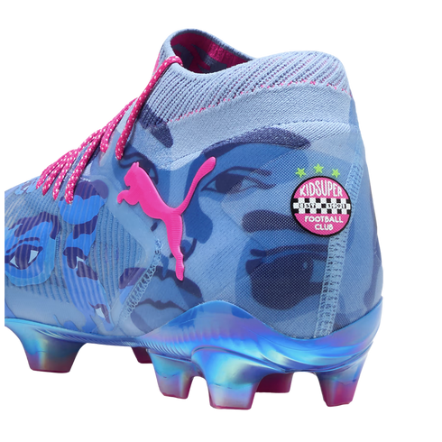 A Puma x KidSuper soccer cleat in light blue with dark blue face graphics, pink accents, and an iridescent sole. A KidSuper Football Club badge is displayed on the heel.
