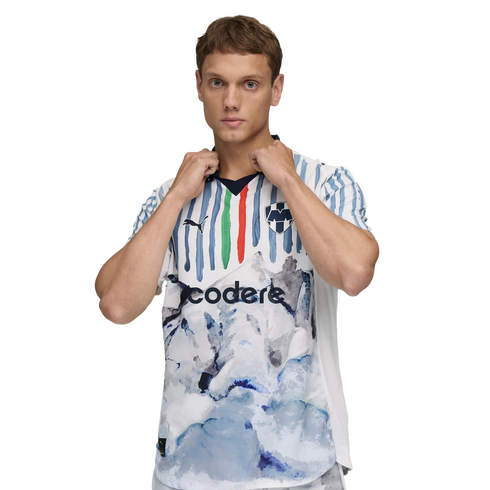 A man modeling a white soccer jersey featuring blue, green, and red vertical stripes and a large blue and white watercolor graphic on the lower half.