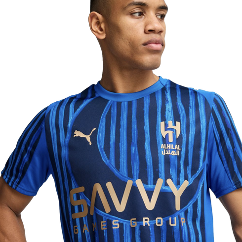 A young man wearing a blue Puma Al-Hilal soccer jersey with "SAVVY GAMES GROUP" printed on the chest.