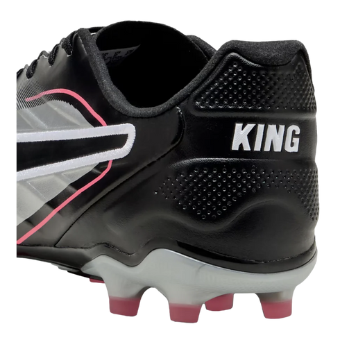 A close-up of the heel of a black PUMA King soccer cleat, featuring silver and pink accents, white "KING" branding, and pink-tipped studs.
