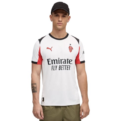 A man wearing a white Puma AC Milan soccer jersey with red accents, a black cap, and olive green pants against a black background.