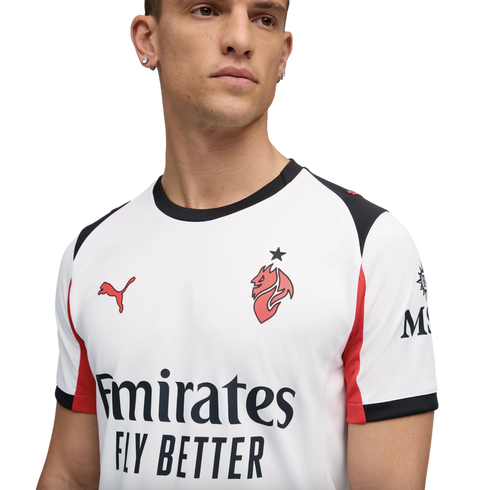 A man models a white AC Milan football jersey by Puma, featuring red and black accents and the "Emirates FLY BETTER" sponsor logo, against a solid black background.
