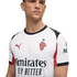 A man models a white AC Milan football jersey by Puma, featuring red and black accents and the "Emirates FLY BETTER" sponsor logo, against a solid black background.