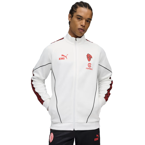 A man wearing a white Puma KING track jacket with red accents and black AC Milan pants against a black background.