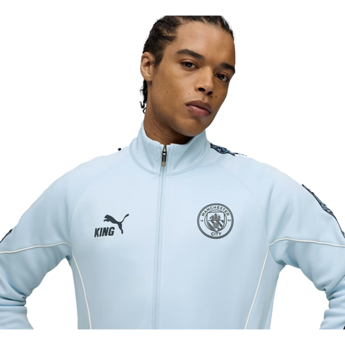 A man in a light blue Manchester City zip-up jacket with the Puma logo and club crest against a black background.