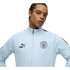 A man in a light blue Manchester City zip-up jacket with the Puma logo and club crest against a black background.