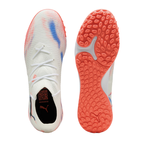 Top and sole view of a white Puma turf soccer shoe with pink and blue accents. It features a white knitted upper, sock-like collar, and a textured orange rubber outsole.