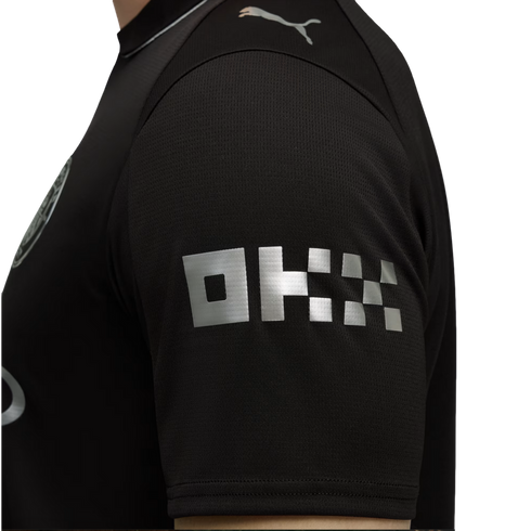 Close-up of a black jersey sleeve with a silver blocky "OKX" logo and a silver Puma logo on the shoulder.
