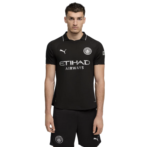 A man wearing a black Manchester City soccer kit with silver logos and sponsors, set against a solid black background.