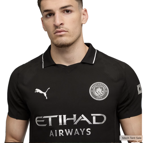 A young man wearing a black Manchester City soccer jersey with silver club crest, Puma, and Etihad Airways logos.