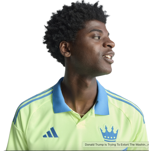 Profile of a smiling young Black man with an afro wearing a lime green Adidas polo shirt with a blue collar and crown logo, against a black background.