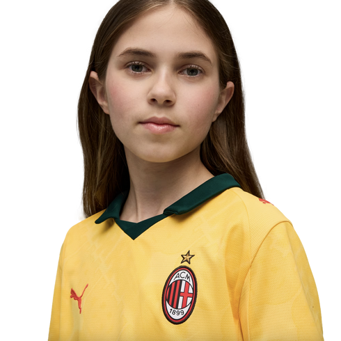 A portrait of a young person with long brown hair wearing a yellow AC Milan soccer jersey against a solid black background.