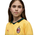 A portrait of a young person with long brown hair wearing a yellow AC Milan soccer jersey against a solid black background.