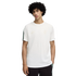 A curly-haired man stands against a black background wearing a white Puma short-sleeved t-shirt and dark trousers with patterned side details.