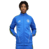 Young man with dreadlocks wearing a blue Manchester City tracksuit featuring a Puma logo and club crest, standing against a black background.