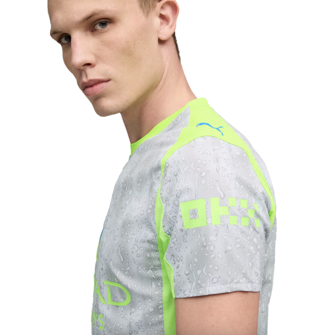 A fair-skinned man with blond hair wears a grey and lime green Puma sports jersey featuring a water droplet pattern and sponsorship branding.