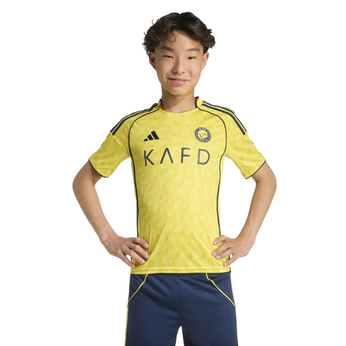 A young Asian male wearing a yellow Al-Nassr football jersey stands with hands on his hips against a black background.