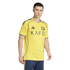 A man modeling a yellow soccer jersey with navy blue trim and "KAFD" across the chest, paired with navy blue shorts. The jersey features a subtle wavy pattern.