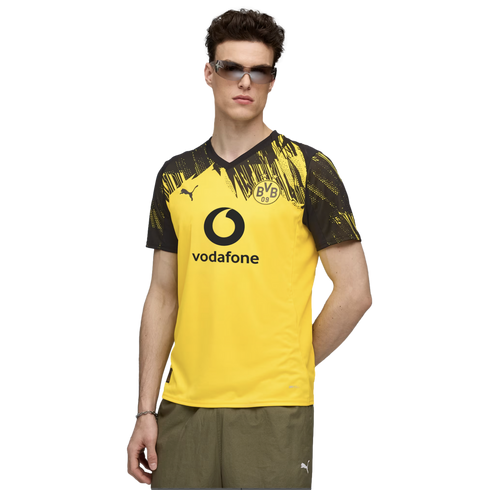 A man wearing a yellow and black Borussia Dortmund soccer jersey with a Vodafone logo, sunglasses, and olive shorts.