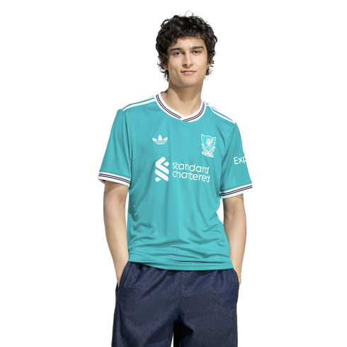 A man wearing a turquoise Liverpool FC jersey and dark blue shorts, standing against a black background.
