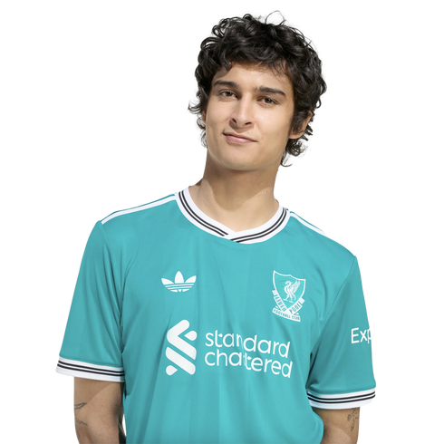 A young man with dark, wavy hair wears a teal Liverpool F.C. jersey against a solid black background.