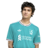 A young man with dark, wavy hair wears a teal Liverpool F.C. jersey against a solid black background.