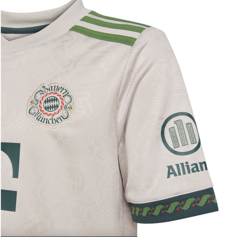 Close-up of a white FC Bayern Munich soccer jersey featuring an intricate woven pattern, vintage-style crest, green shoulder stripes, and Allianz sleeve logo.