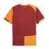 The back of a maroon and orange Puma football jersey with split-color panels and shoulder logos. A small Turkish phrase is printed below the orange collar.