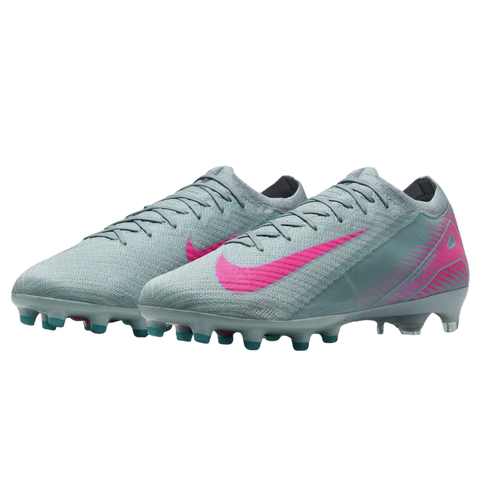 A pair of light grey Nike soccer cleats featuring vibrant pink swooshes and pink geometric patterns on the heels. The sole has teal and white studs, shown against a black background.