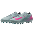 A pair of light grey Nike soccer cleats featuring vibrant pink swooshes and pink geometric patterns on the heels. The sole has teal and white studs, shown against a black background.