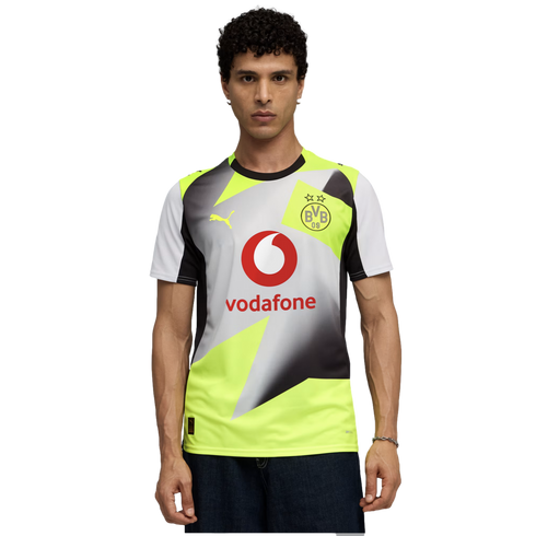 Man with curly hair wearing a yellow and grey geometric Puma BVB soccer jersey with a red Vodafone logo, set against a solid black background.
