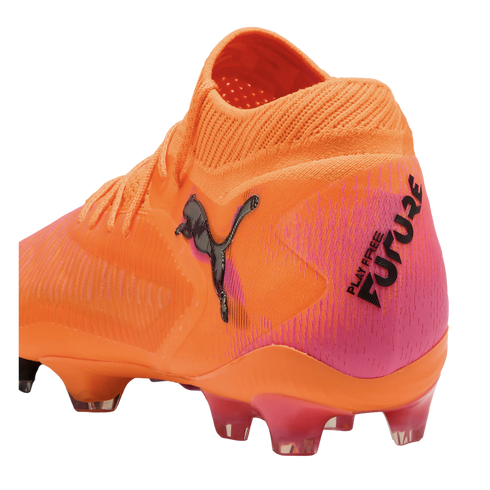An orange and pink Puma Future soccer cleat with a textured upper, black Puma logo, and "PLAY FREE FUTURE" text on the heel.