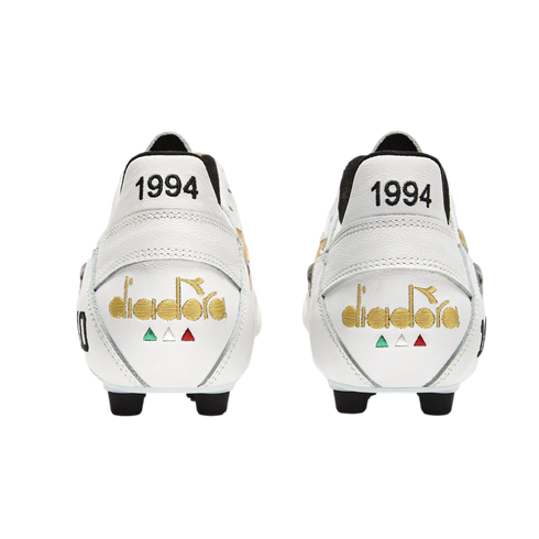 Rear view of two white leather soccer cleats featuring gold embroidered Diadora logos and the year '1994' in black on the heels, set against a solid black background.